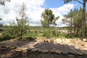 A natural landscape with a stone wall, trees, and a distant view of a residential area. - House with a garden near Pézenas, between the sea and the mountains (Neffiès)