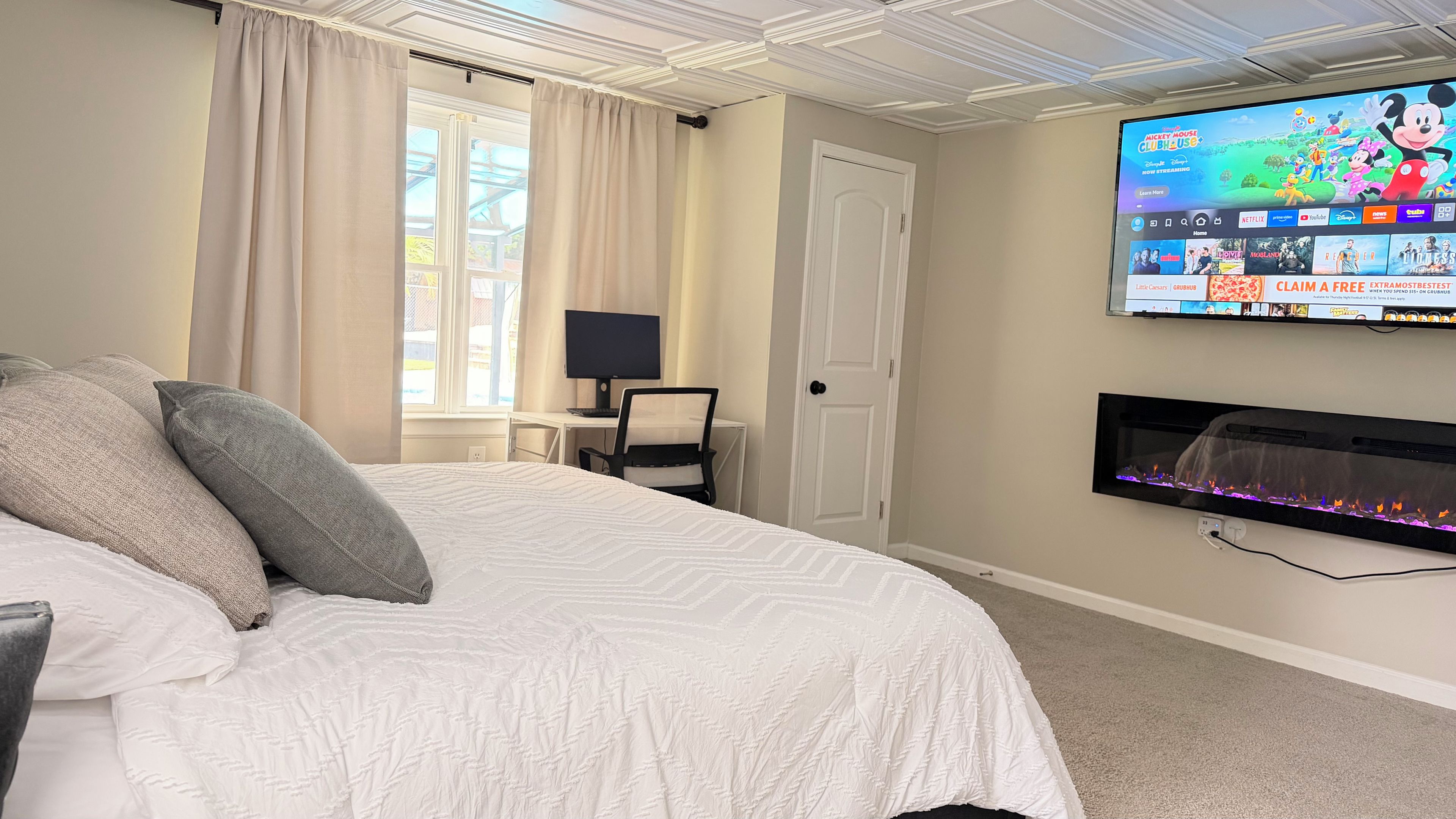 A hotel room with a bed, a desk with a computer, a television, and a fireplace.