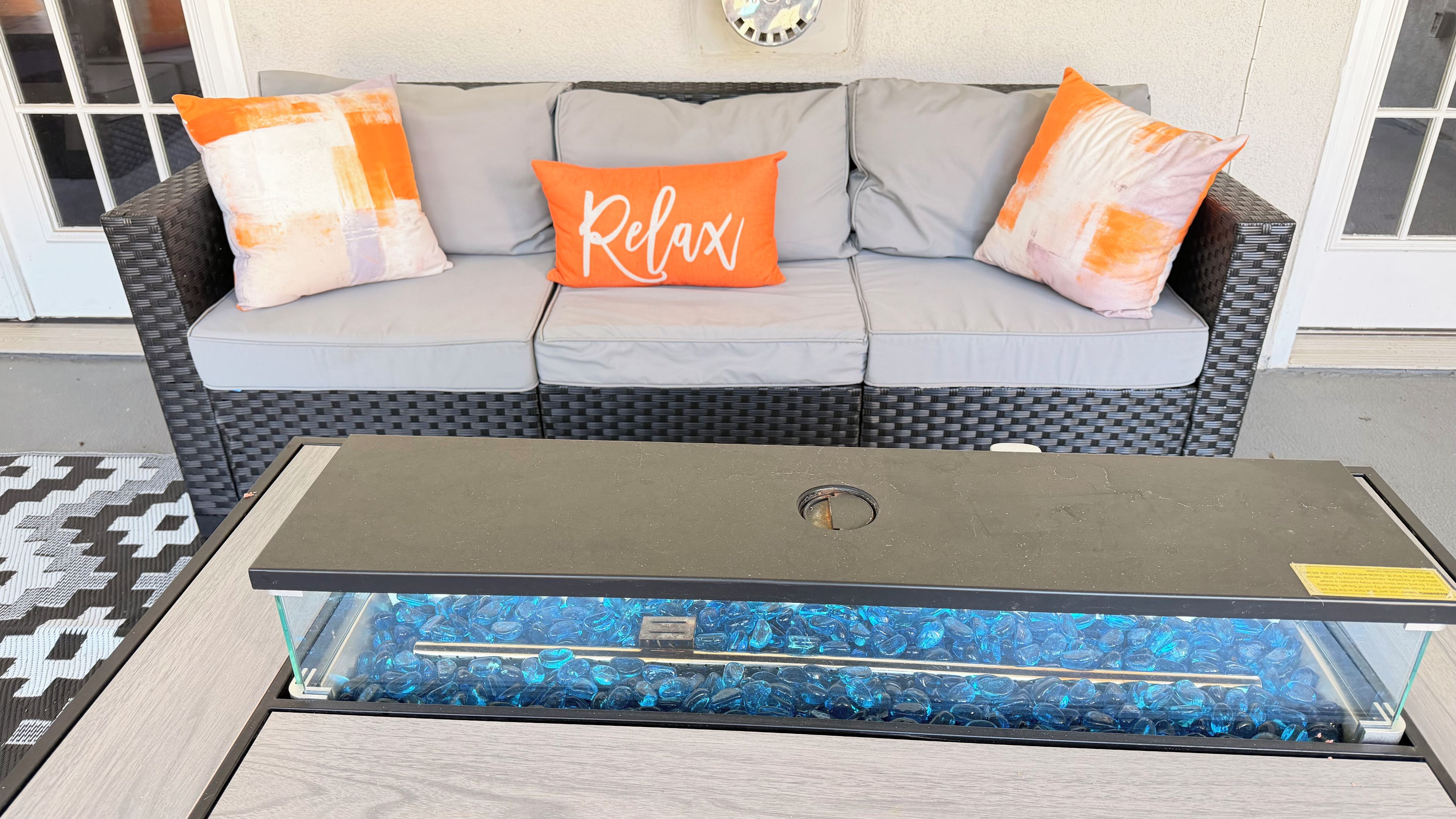 A room with a grey sofa, orange pillows, and a glass-top coffee table with blue glass pebbles.