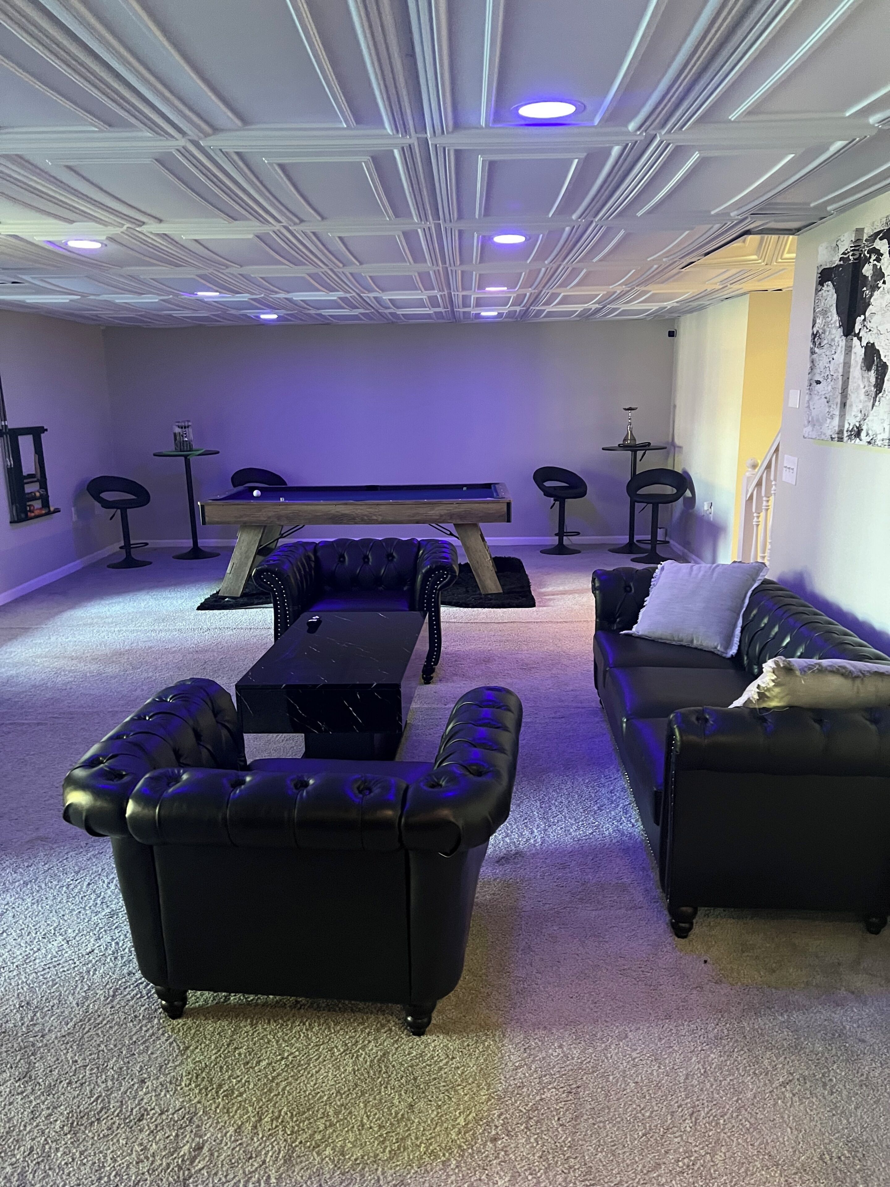 A room with a pool table, two leather sofas, a small table, and a bar area.