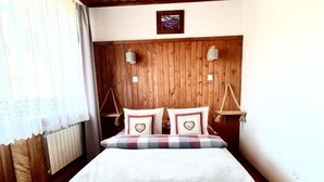 Teto de madeira, cama com travesseiro xadrez e parede branca.