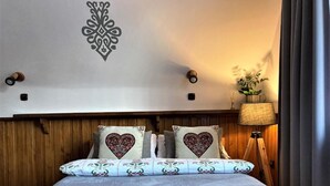 Uma cama com roupa de cama estampada, um objeto decorativo na parede e um abajur com uma planta.