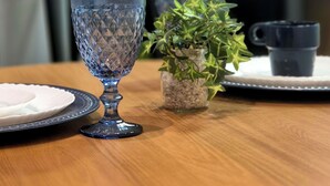 Una mesa redonda de madera con un vaso azul, una pequeña planta en maceta y una taza negra.
