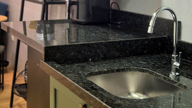 Una cocina con encimera de granito, pileta de acero inoxidable y microondas en un estante.