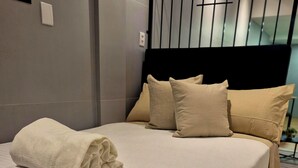 Una cama bien hecha con una toalla blanca doblada, un cabecero con varios almohadones y un diseño moderno.