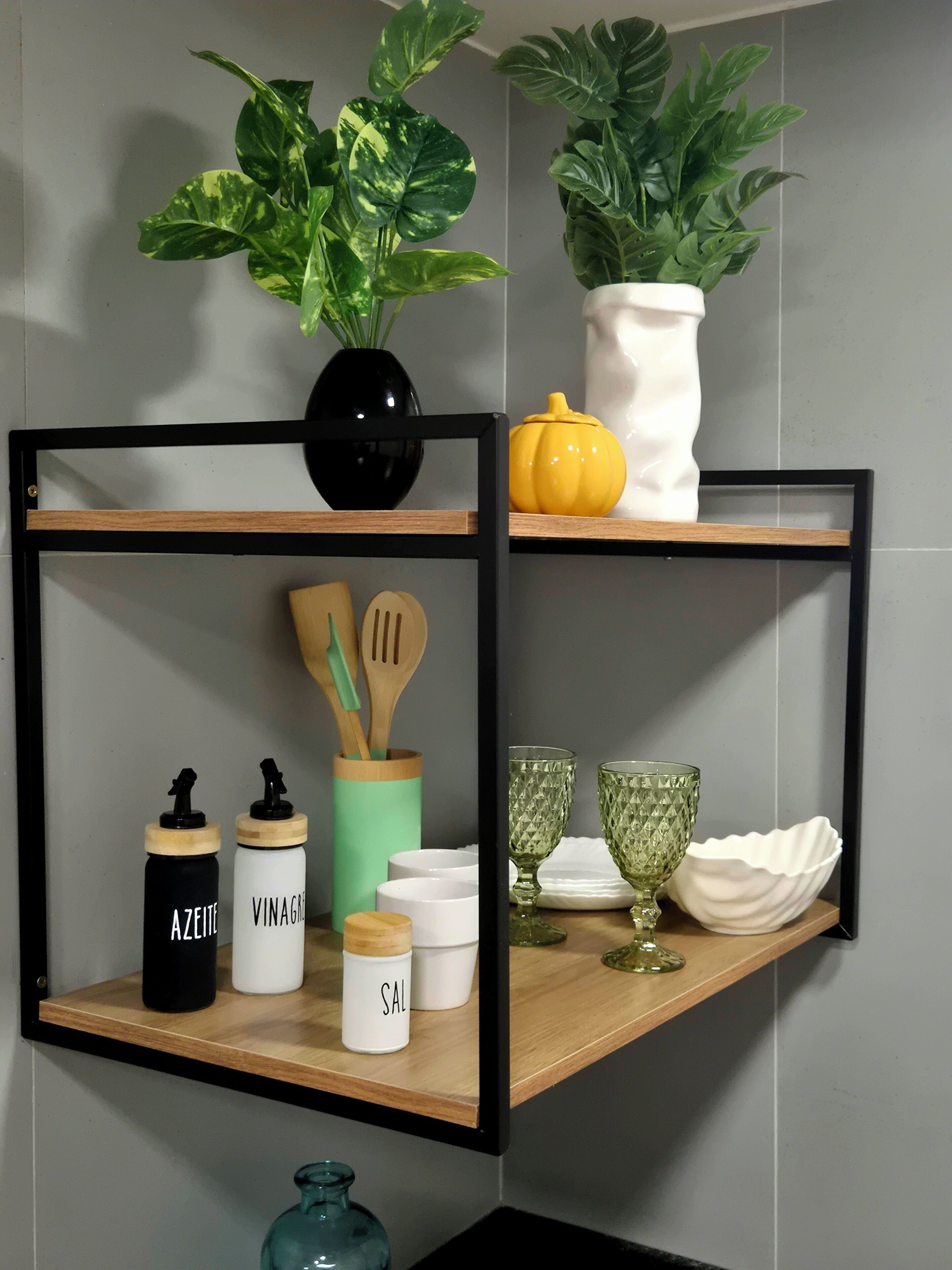 Une étagère de cuisine avec un vase noir, une citrouille jaune, des ustensiles de cuisine en bois et de la verrerie.