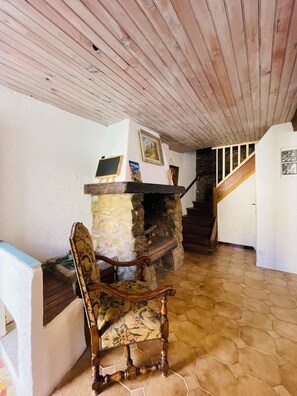 Ein Kamin aus Stein, ein Holzstuhl, eine Treppe und eine weiße Wand mit einem gerahmten Bild.