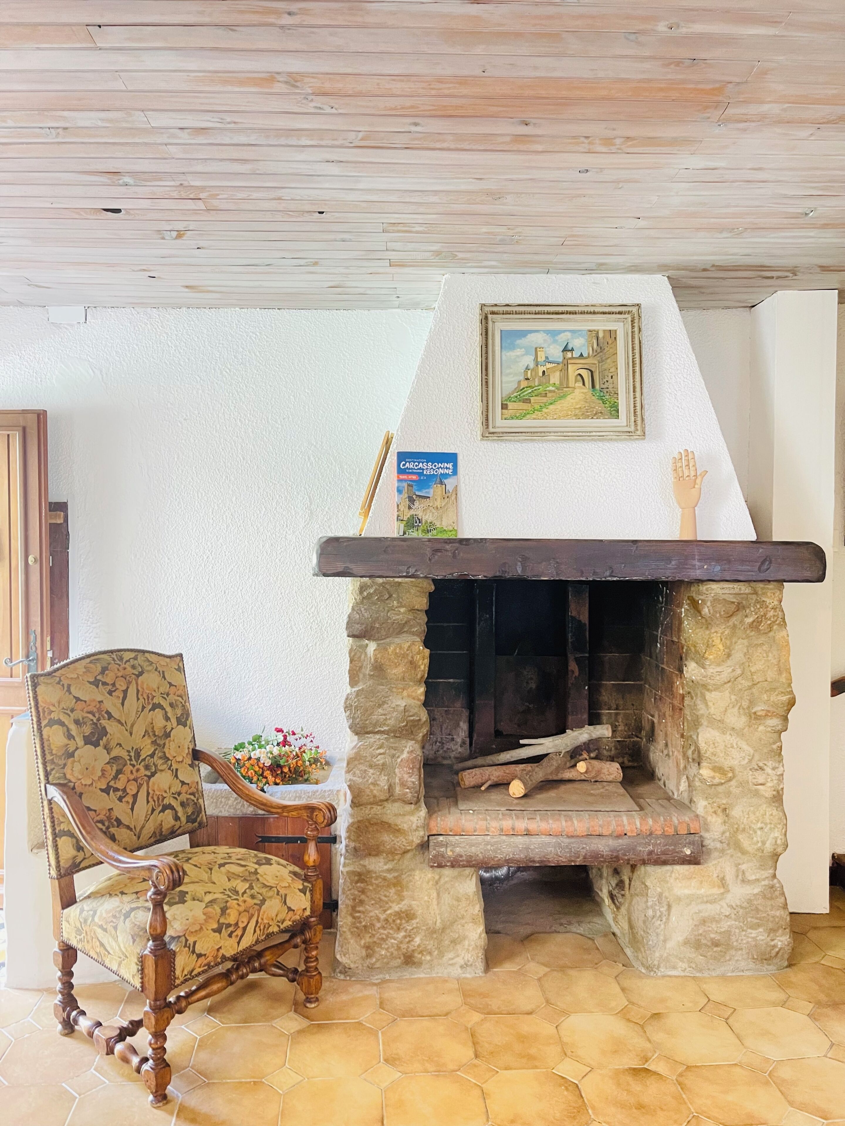 A stone fireplace with a mantel, a framed picture above it, and a chair with a floral pattern.