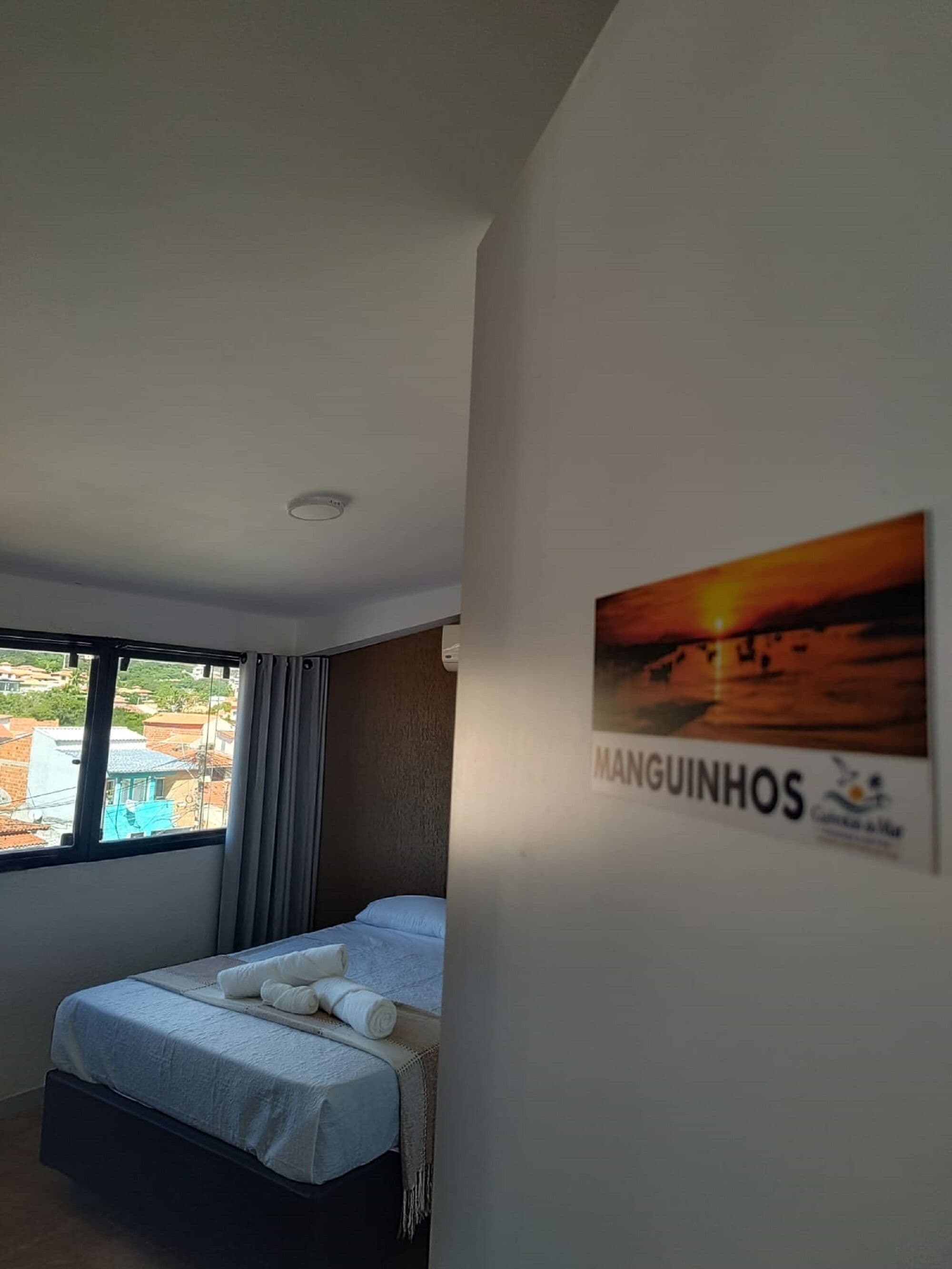 A hotel room with a bed, a window with curtains, a wall-mounted picture, and a ceiling light.