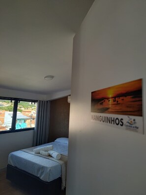 Quarto de hotel com cama, janela com cortinas, quadro na parede e luminária no teto.