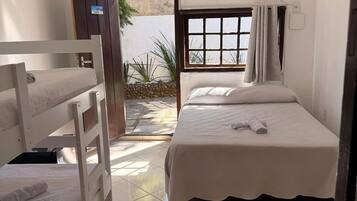 Quarto com beliches, janela com cortinas, piso em azulejos e porta que dá para o exterior.