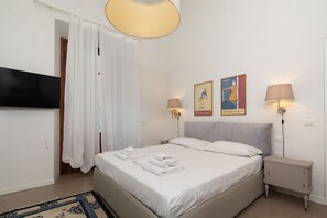 Un dormitorio con cama, dos lámparas de noche, televisor montado en la pared y una puerta con cortina.