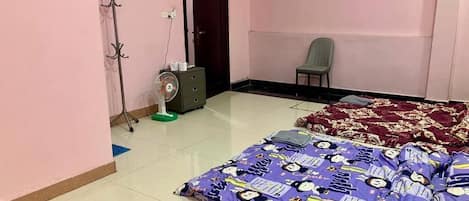 A room with two beds, a chair, a coat rack, a fan, and a door.