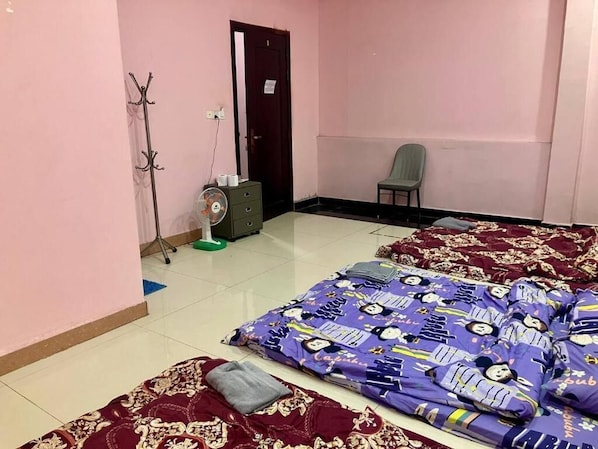 A room with two beds, a chair, a coat rack, a fan, and a door.