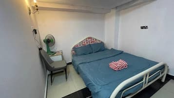 A single bed with a metal frame, a bedside table with a lamp, and a wall-mounted fan.