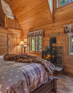 A cabin interior with a bed, a fireplace, a window, and a door. - Dancing Cubs Cabin!  Hot Tub, Walk to Beach! (Homewood)