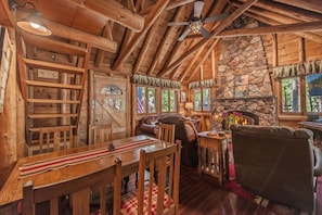 A rustic cabin interior with a stone fireplace, wooden furniture, and a ceiling fan. - Dancing Cubs Cabin!  Hot Tub, Walk to Beach! (Homewood)