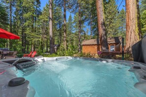 Un jacuzzi rodeado de altos árboles, una cabaña de madera y sillas rojas.