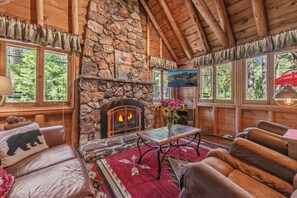A cozy cabin interior with a stone fireplace, leather furniture, and large windows. - Dancing Cubs Cabin!  Hot Tub, Walk to Beach! (Homewood)