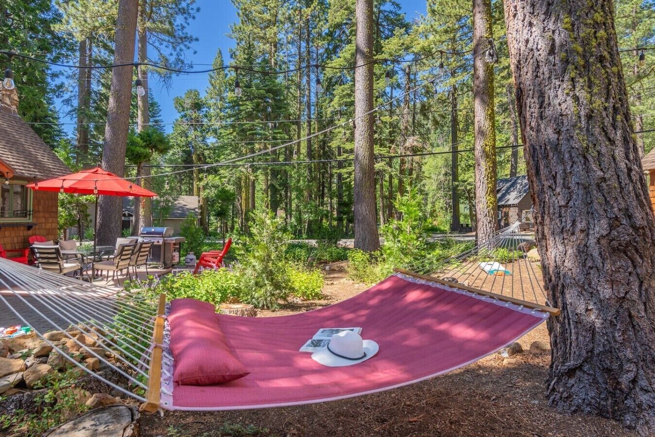 A hammock in a forested area with a red canopy and a dining table with chairs.