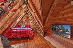 A cozy cabin bedroom with a wooden ceiling, a bed with a red plaid bedspread, a welcome sign, and a window with a scenic view. - Dancing Cubs Cabin!  Hot Tub, Walk to Beach! (Homewood)