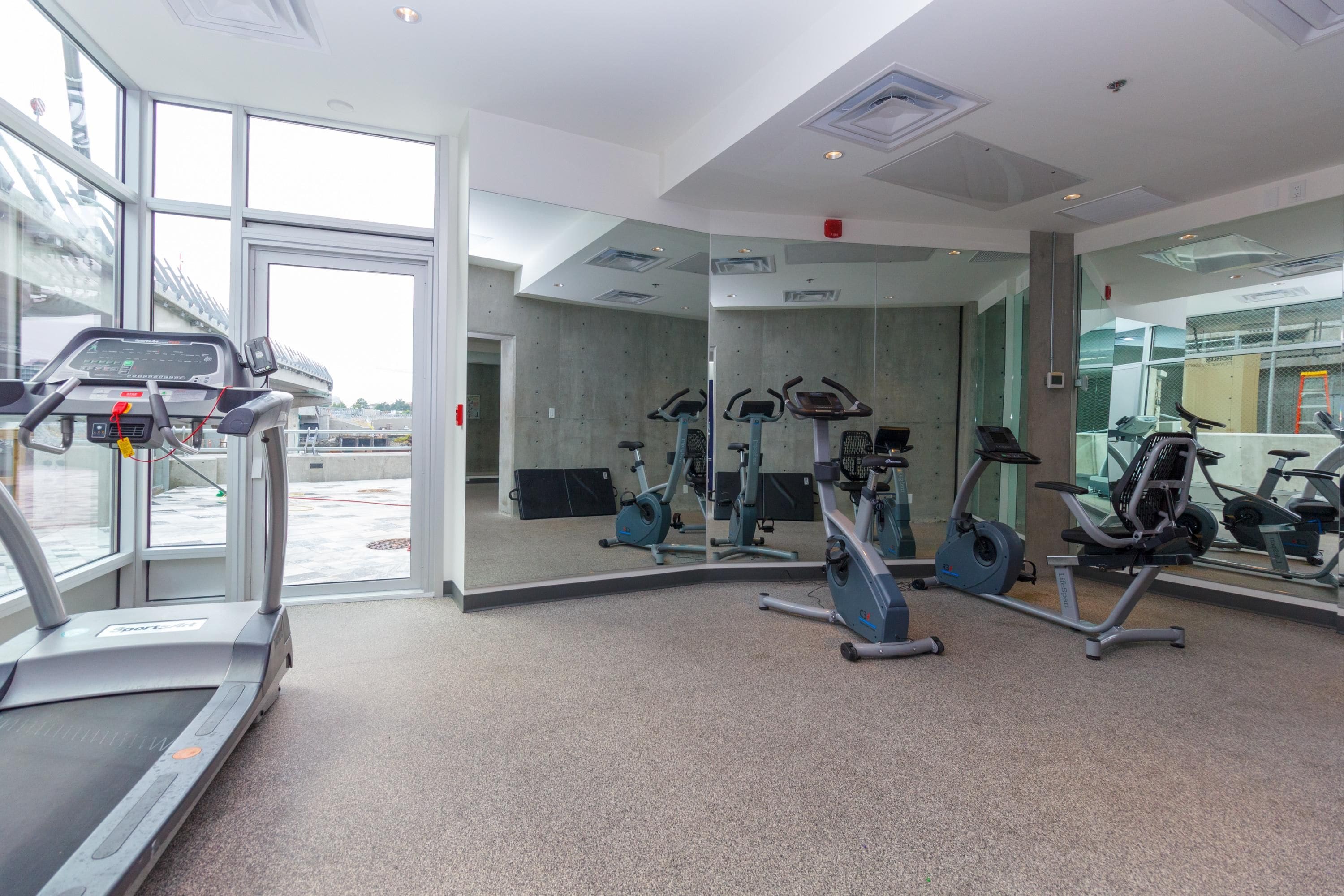 A gym with cardio machines, mirrors, and a large window.