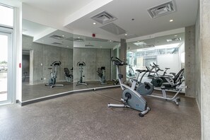 Un gimnasio con diverso equipo de ejercicio, un espejo grande y suelo de hormigón.