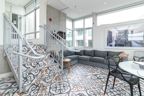 Un interior moderno con una escalera, un sofá gris y baldosas de suelo con diseño.
