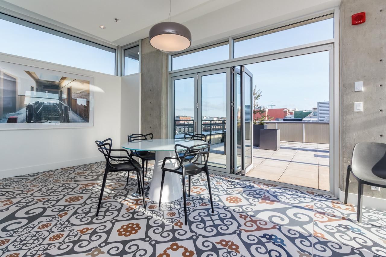 Ein modernes Interieur mit einem Glastisch und Stühlen, einem gemusterten Boden und Blick durch große Fenster.