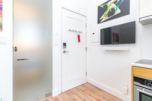 Ein Zimmer mit weißer Tür, einem montierten Fernseher, einem roten Kleiderbügel und einem eingebauten Backofen.