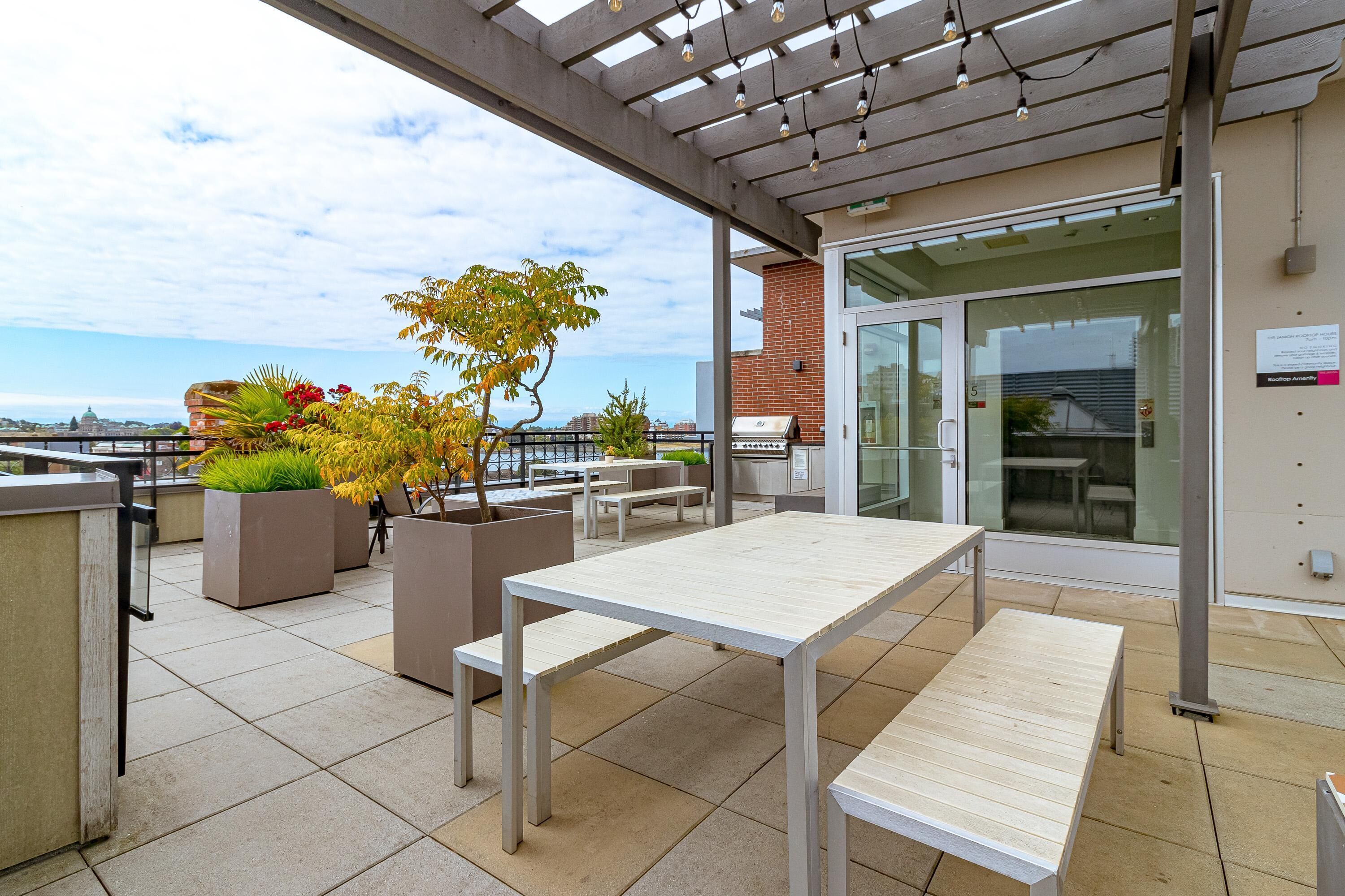 Une terrasse extérieure avec des tables et des chaises, des plantes en pot et une vue sur la ville.