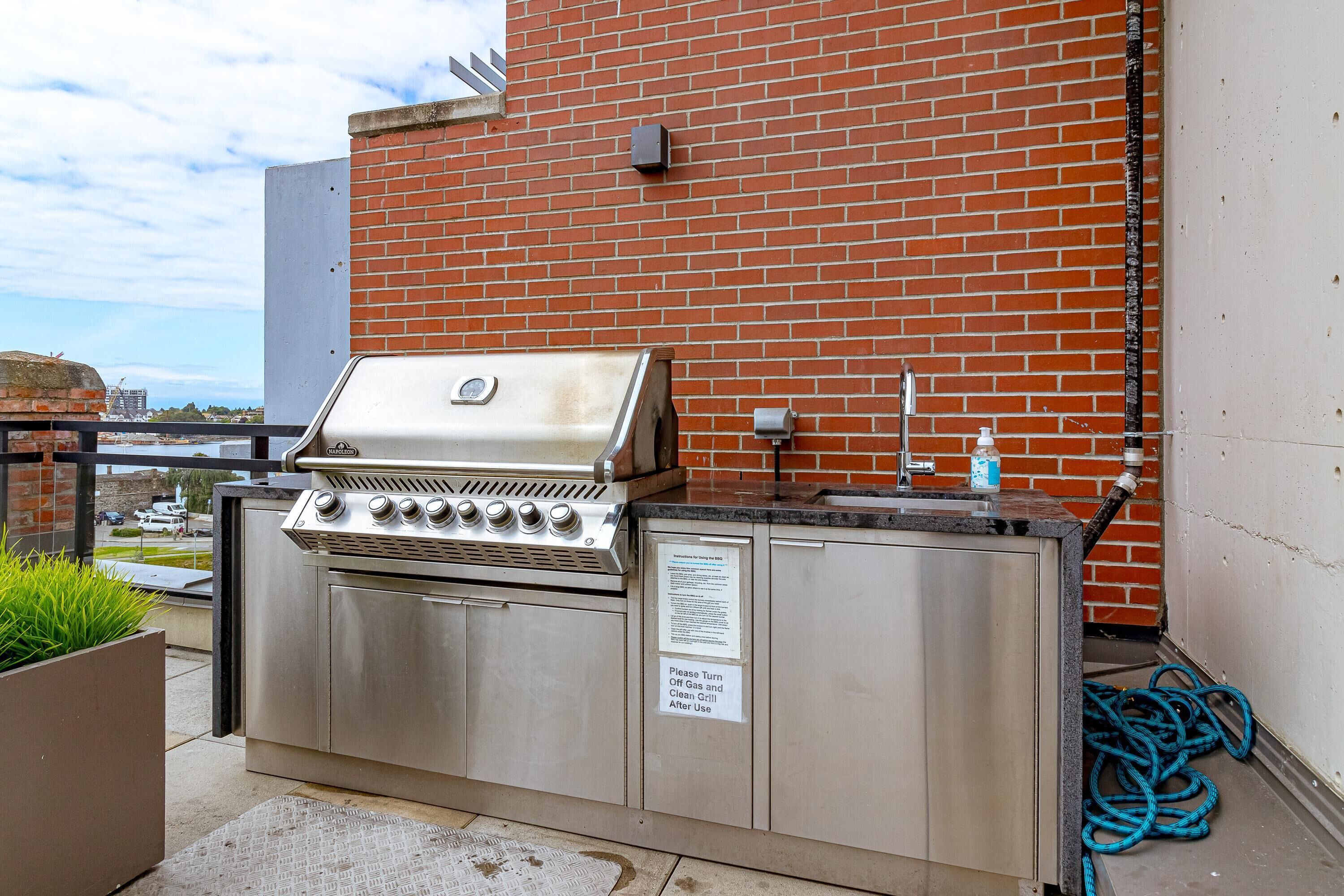 An outdoor grill area with a stainless steel grill, a sink, and a hose.