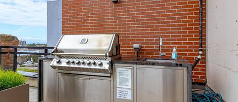 An outdoor grill area with a stainless steel grill, a sink, and a hose.