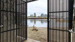 Um portão de metal aberto dá acesso a uma orla com pedriscos e edifícios ao fundo.