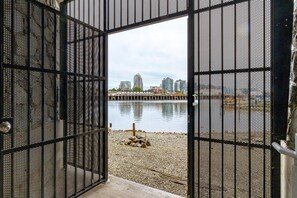Ein offenes Metalltor, das zu einer kiesbestreuten Uferpromenade führt, mit Gebäuden im Hintergrund.