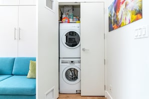 Ein kleiner Hauswirtschaftsraum mit einer Waschmaschine und einem Trockner mit Frontlader, einem blauen Sofa und einem farbenfrohen, abstrakten Gemälde an der Wand.