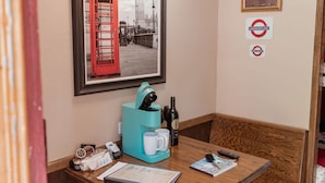 A corner room with a wooden bench, a coffee machine, a framed picture of a red telephone booth, and a ceiling light fixture. - London Calling Railroad Caboose Cabin (Upper Lake)