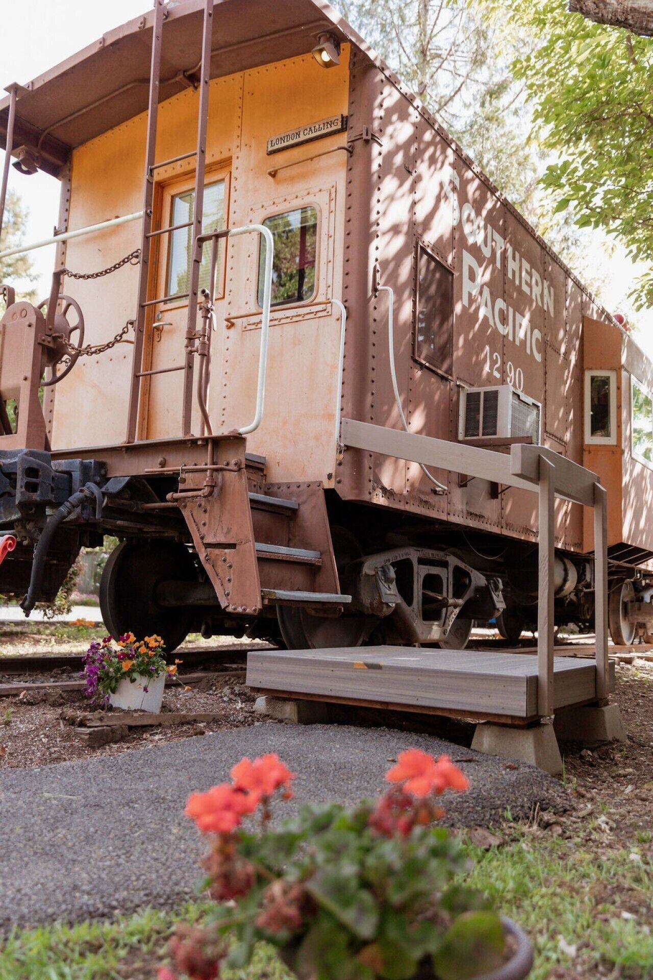 A vintage Southern Pacific train car with a platform and chain mechanism, surrounded by greenery.