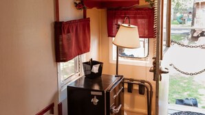 A narrow hallway with a radiator, a black refrigerator, a red telephone booth decoration, and a window with a view of the outdoors. - London Calling Railroad Caboose Cabin (Upper Lake)