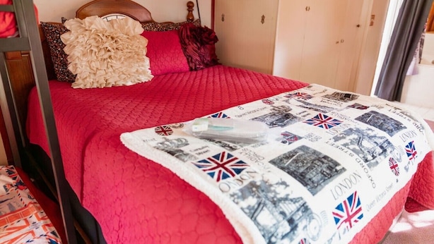 A bed with a red quilt, a decorative pillow, and a blanket with a UK map design. - London Calling Railroad Caboose Cabin (Upper Lake)
