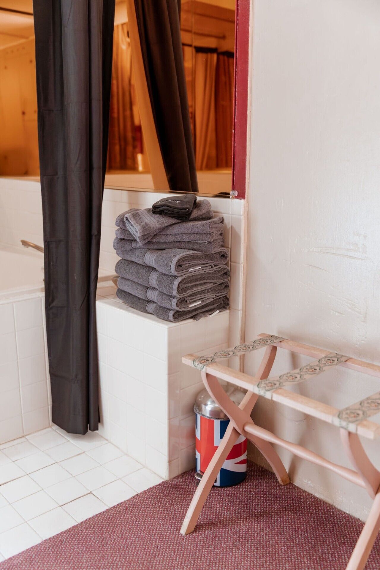 A bathroom with a towel rack, a small wooden stool, and a canister with a flag design.