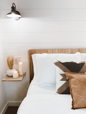 Ein ordentlich bezogenes Bett mit weißer Bettwäsche, einem Holz-Kopfteil und dekorativen Kissen.