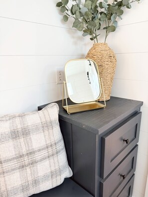 A dark-colored dresser with a mirror on top, a woven basket, and a plant.