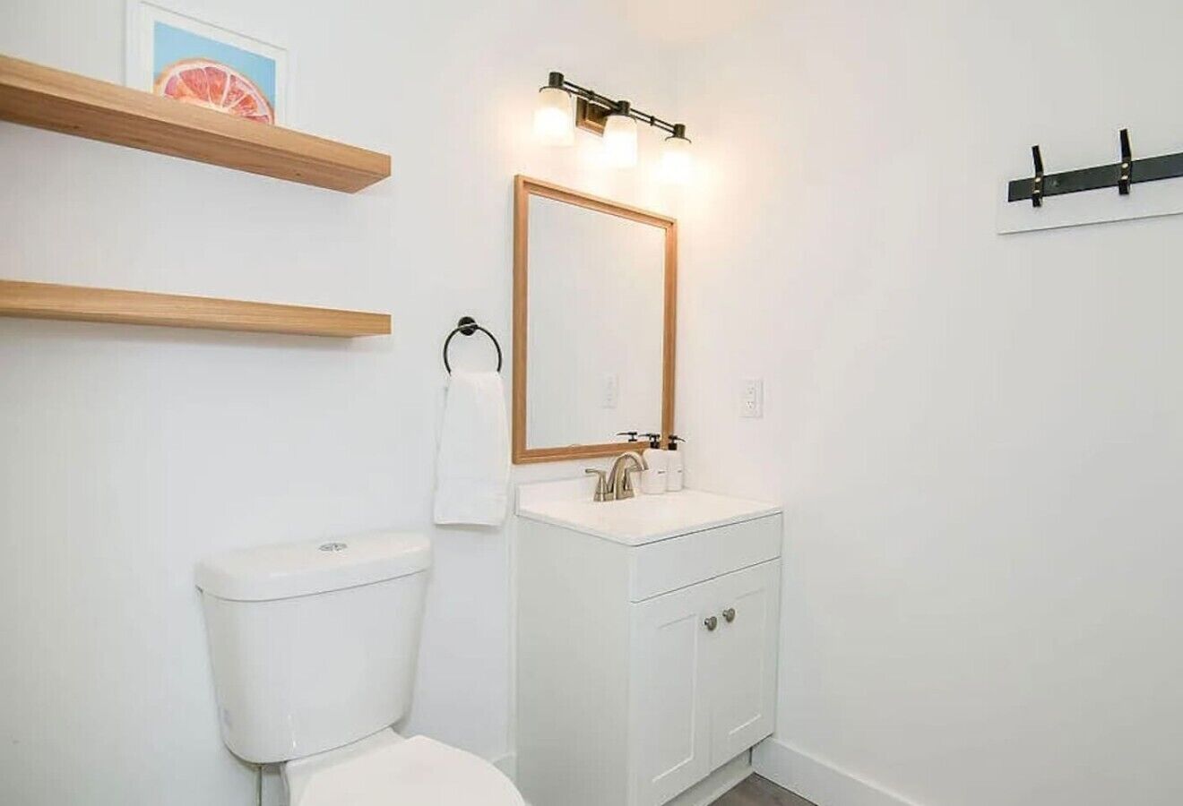 A bathroom with a toilet, sink, mirror, and wooden shelves.