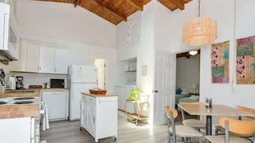 A compact kitchen with white cabinets, a wooden ceiling, and a dining area with a table and chairs.