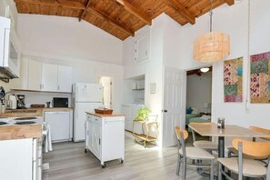A compact kitchen with white cabinets, a wooden ceiling, and a dining area with a table and chairs.