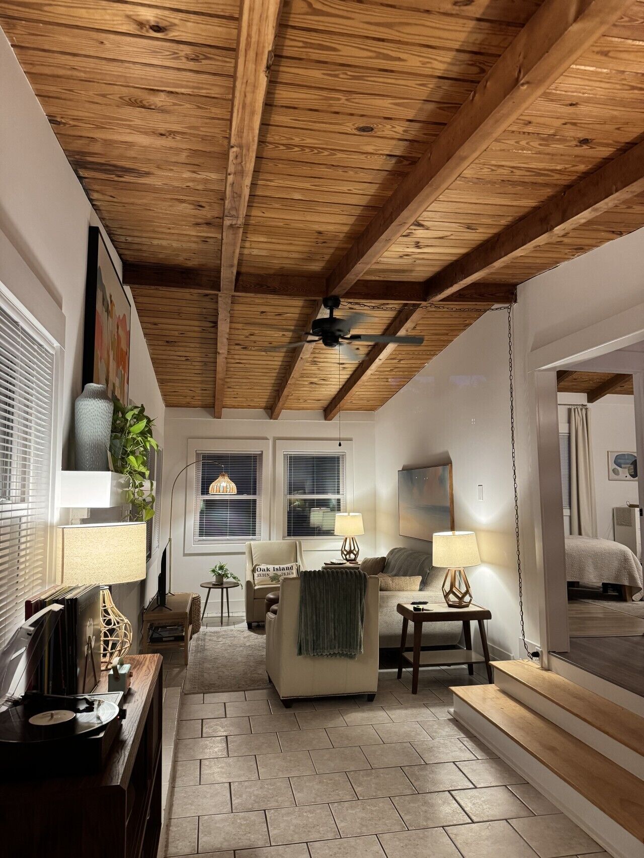 En hyggelig stue med træloft, sofa, lænestol, sofabord og et lille sofabord med lampe.
