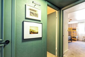 A hallway with green walls, two framed pictures, a door, and a room with bunk beds and a bed.