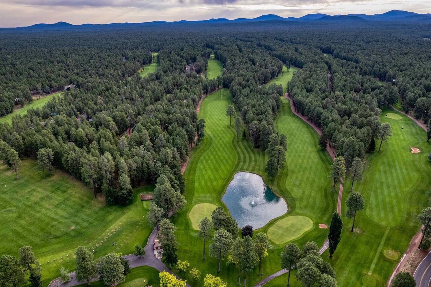 Luchtbeeld van een golfbaan met meerdere greens, een vijver en omliggende beboste gebieden.