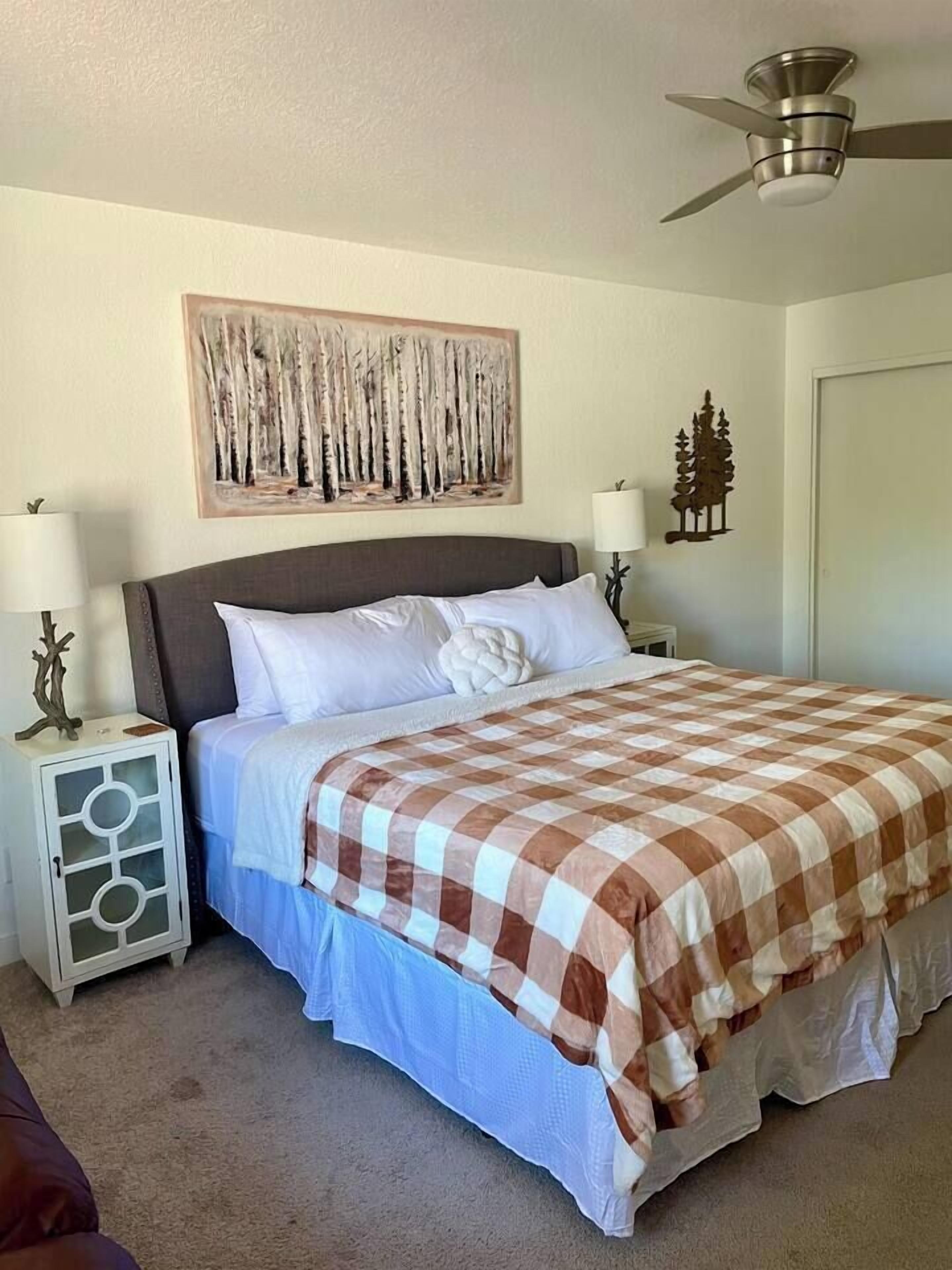 Een slaapkamer met een bed, twee nachtkastjes, een plafondventilator en een kunstwerk aan de muur.